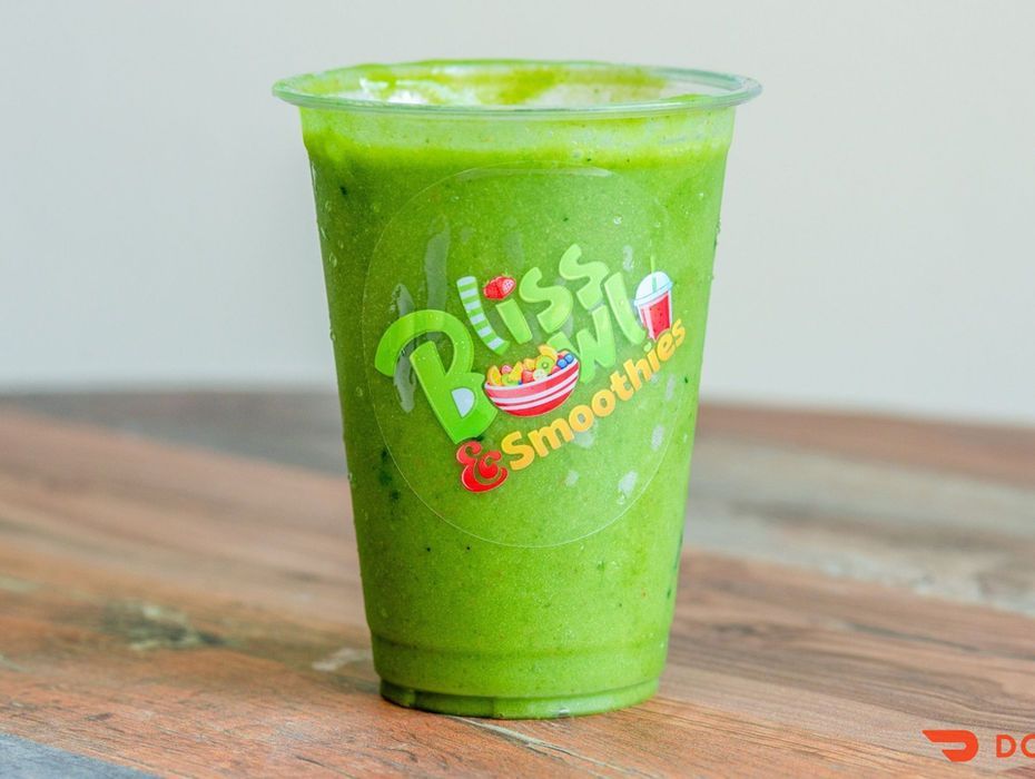 Green smoothie in a clear plastic cup on a wooden table, with a logo on the cup.