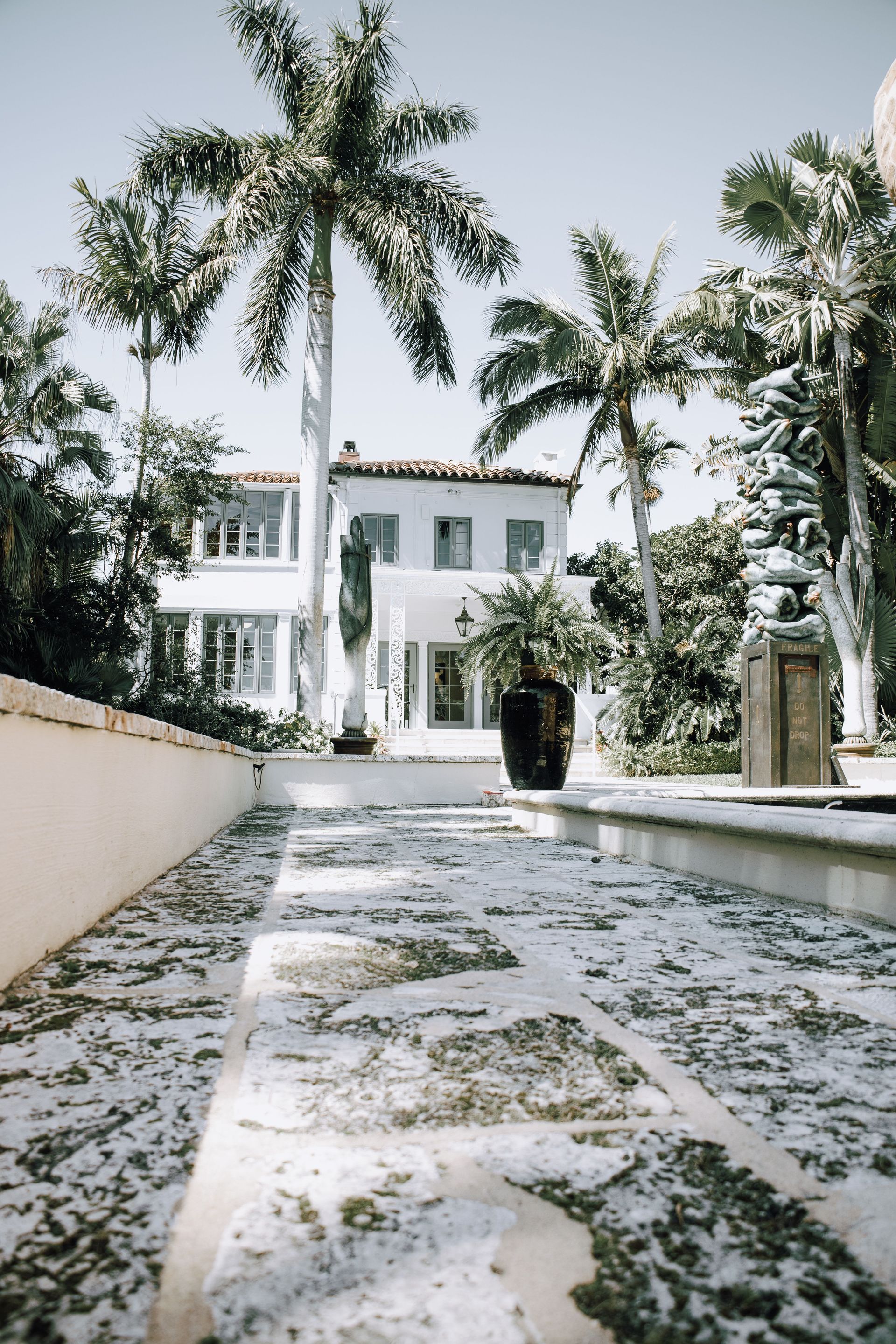 White villa with palm trees and a tiled pathway in a sunny tropical garden