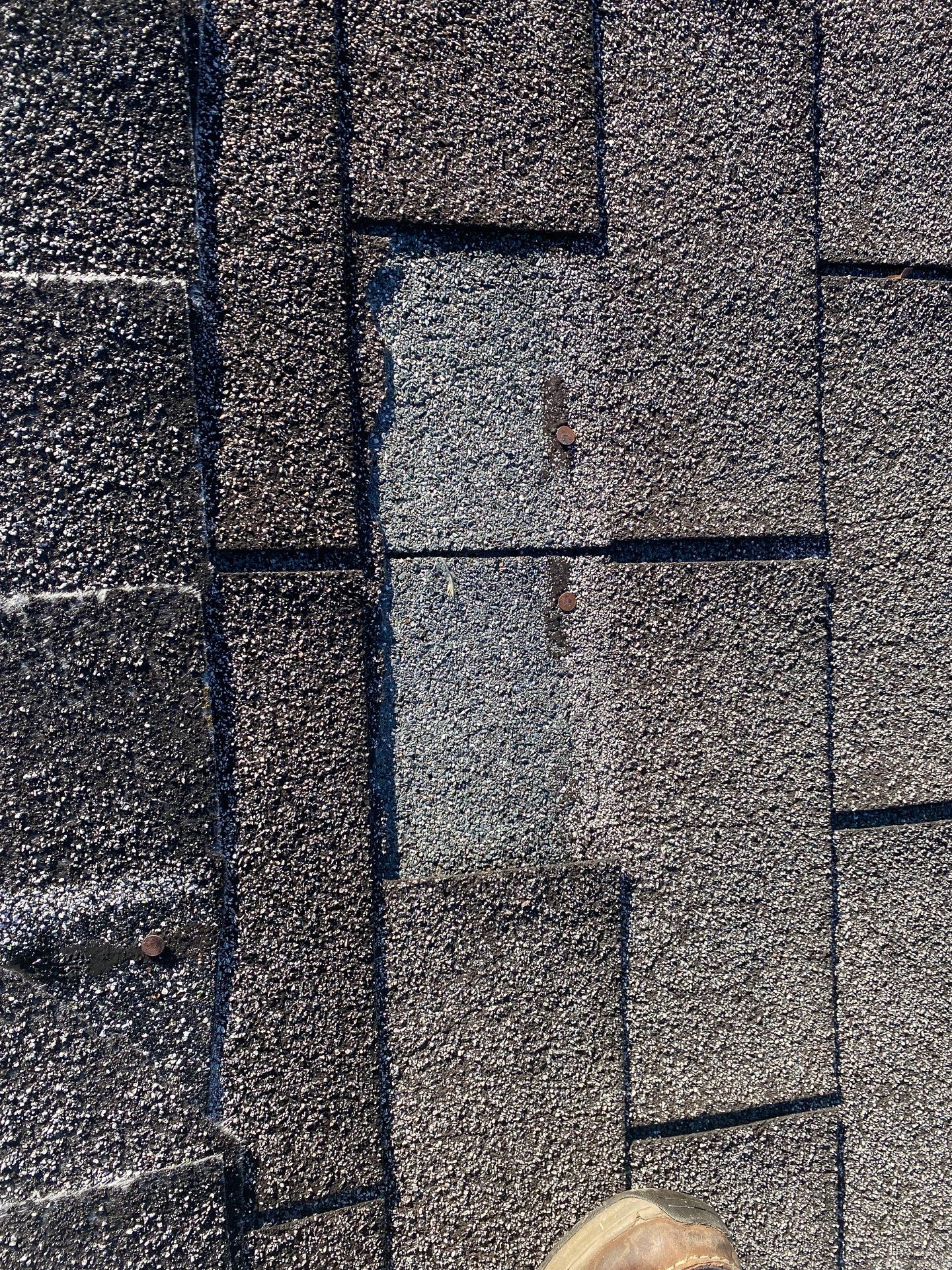 Close-up image of old asphalt shingle roof with missing shingle.