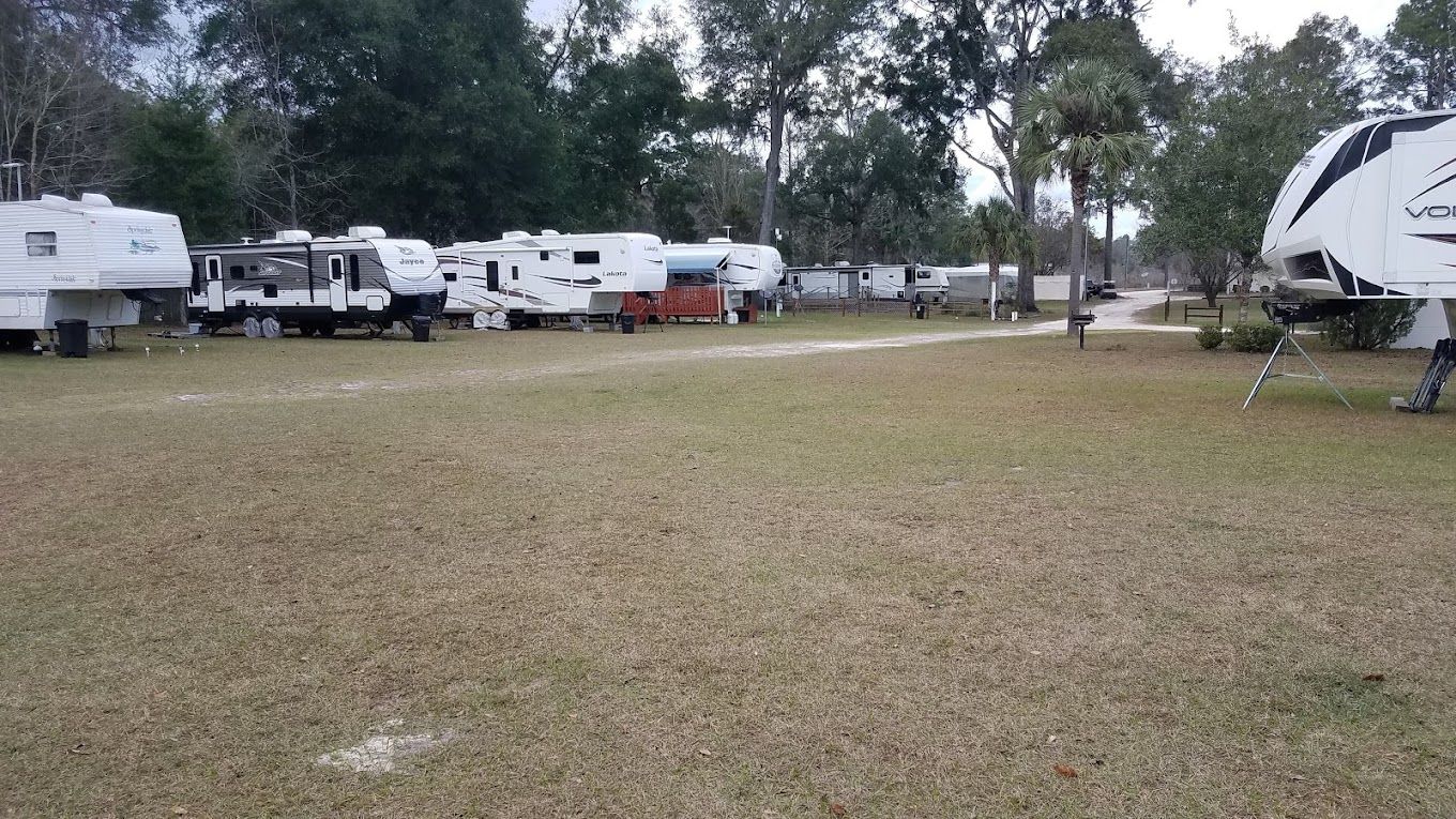 A row of rvs are parked in a grassy field.