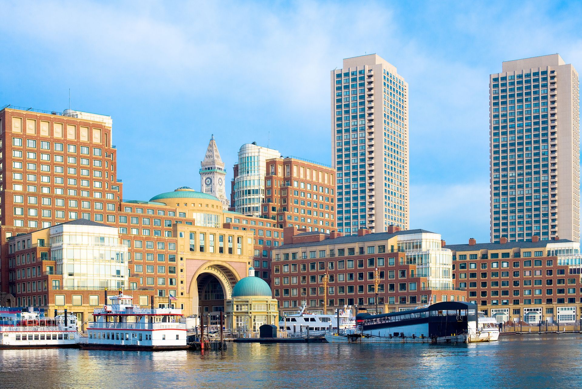 Waterfront city skyline with brick buildings, a stone archway, and tall modern towers reflected in the water