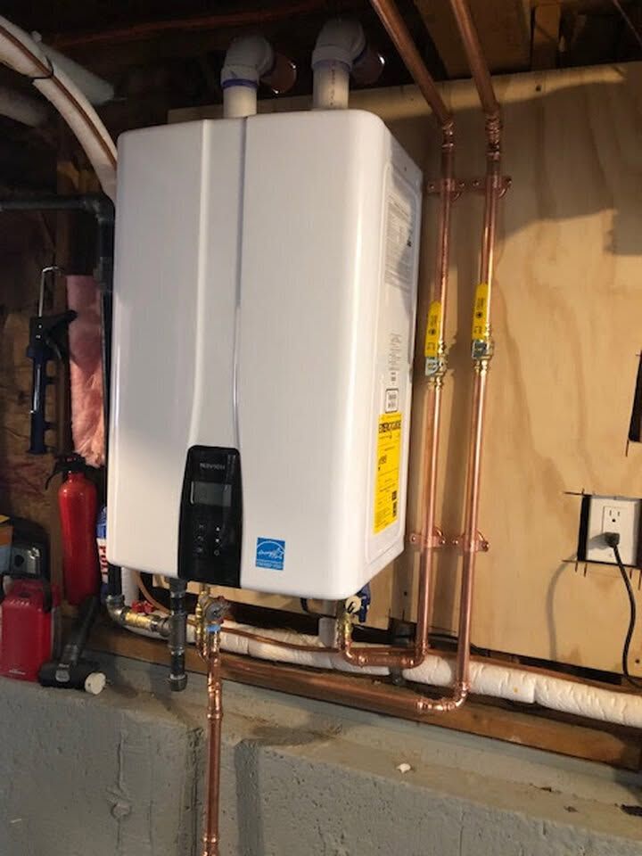 Wall-mounted white tankless water heater with copper pipes in a basement utility area.