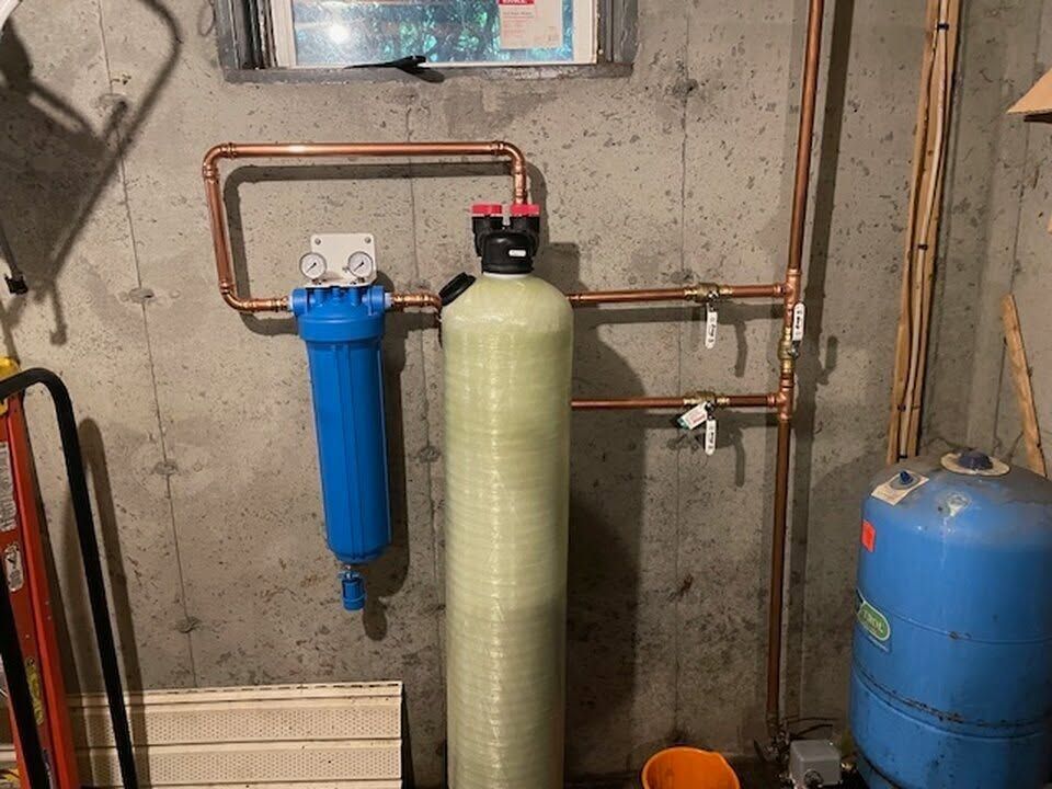 Basement water filtration system with blue and green tanks and copper pipes on a concrete wall