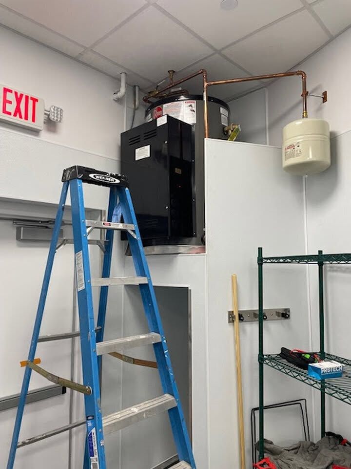 Utility room with blue ladder, open electrical equipment, and exposed wiring near the ceiling.
