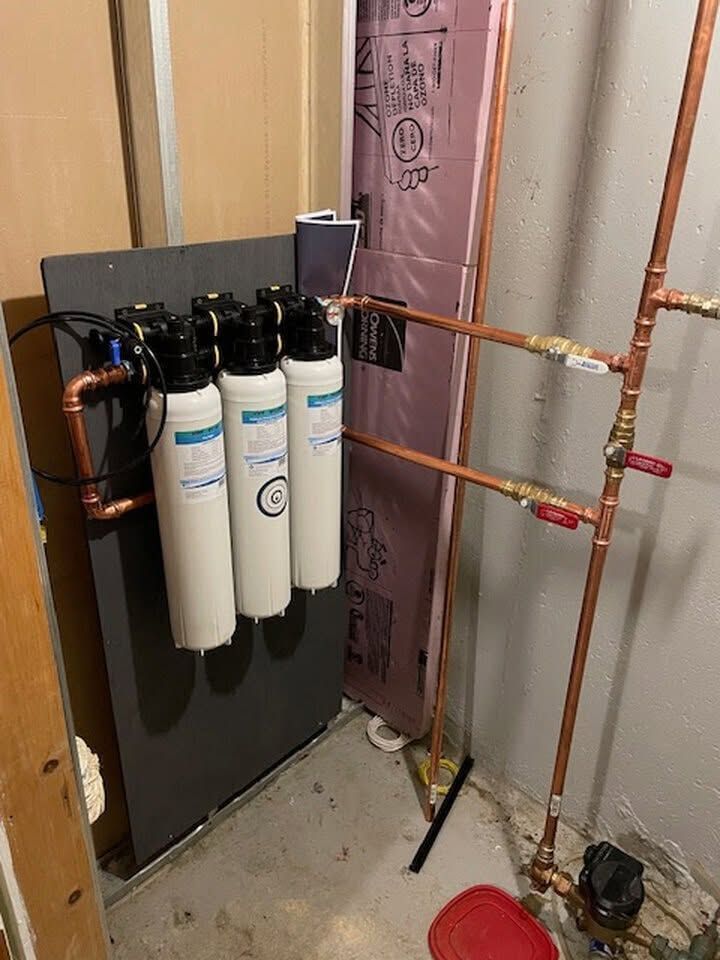 Water filtration system with three white canisters and black tank installed in a utility room.