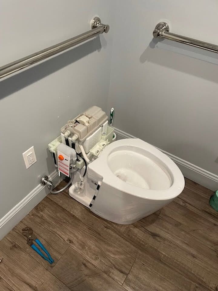 Bathroom with a wall-mounted toilet under repair, exposed plumbing, and grab bars on both sides.