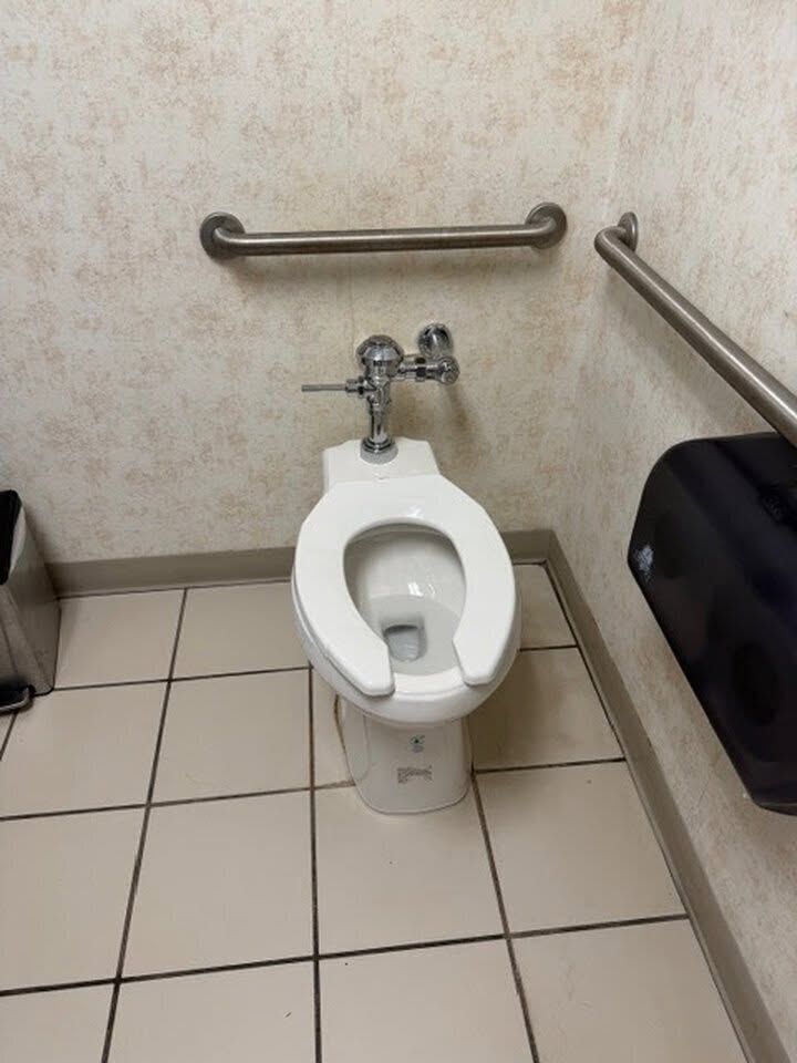 Accessible restroom with a toilet, grab bars, and tiled floor.
