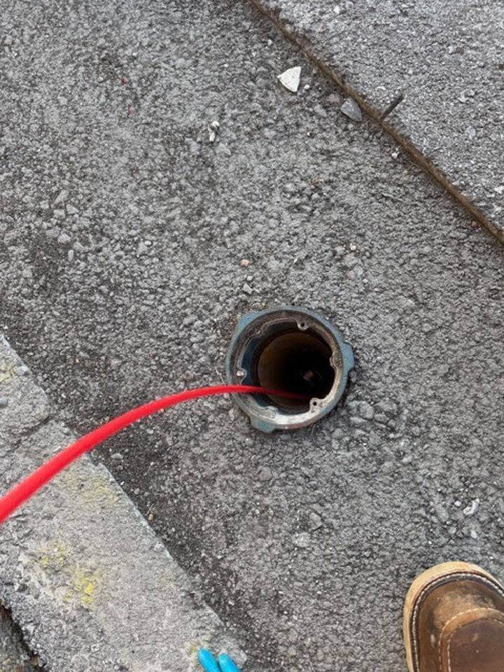 Red cable inserted into a small hole in rough pavement beside a curb and a boot.