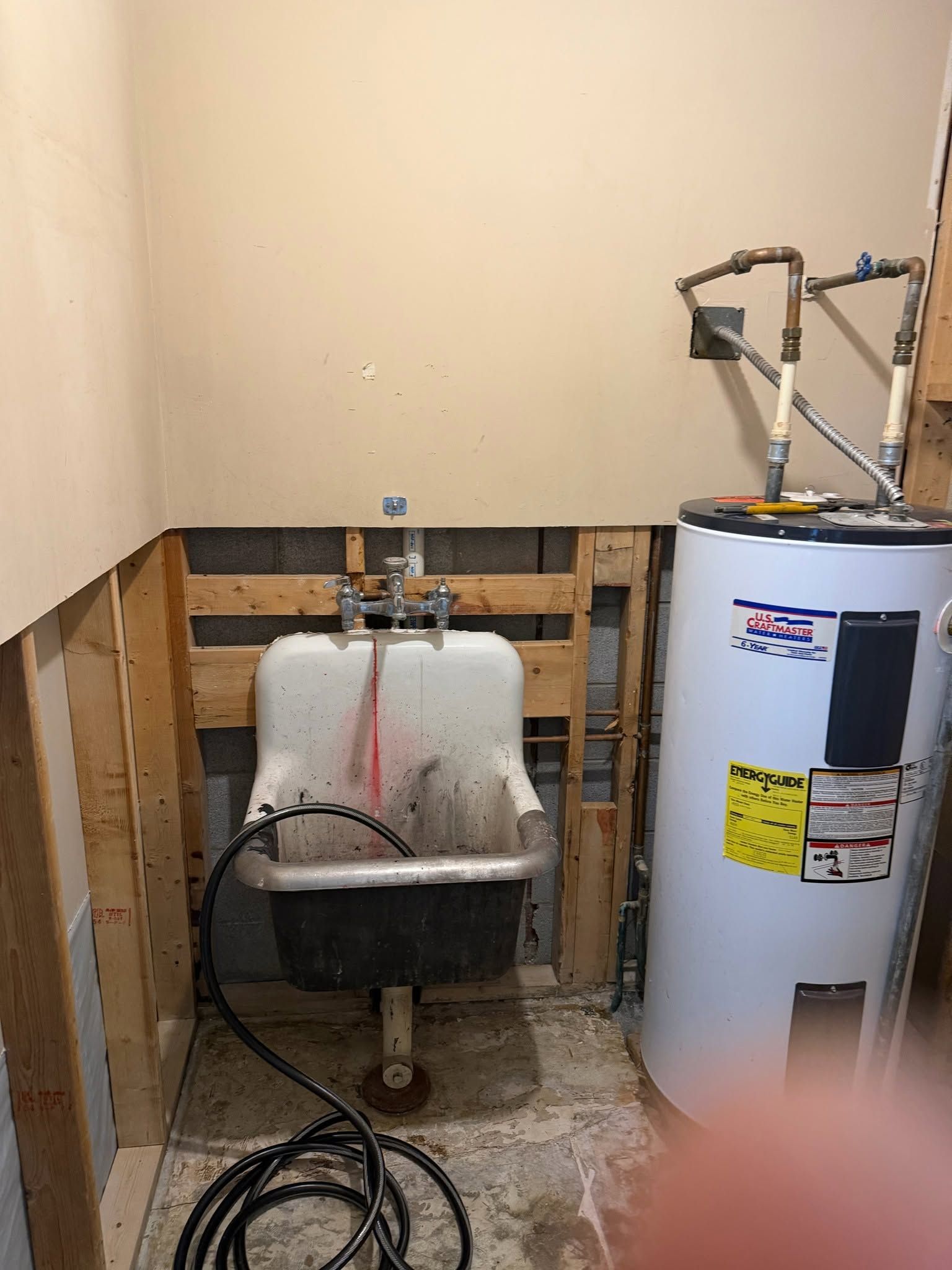 Utility room with a sink and water heater against unfinished walls.