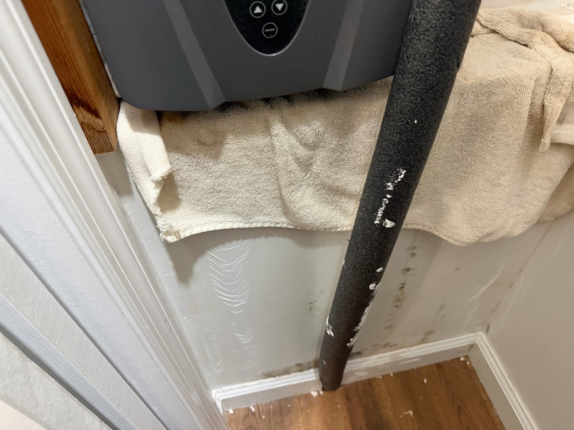 White wall with a black pole leaning against it beside a towel and gray appliance in a corner.