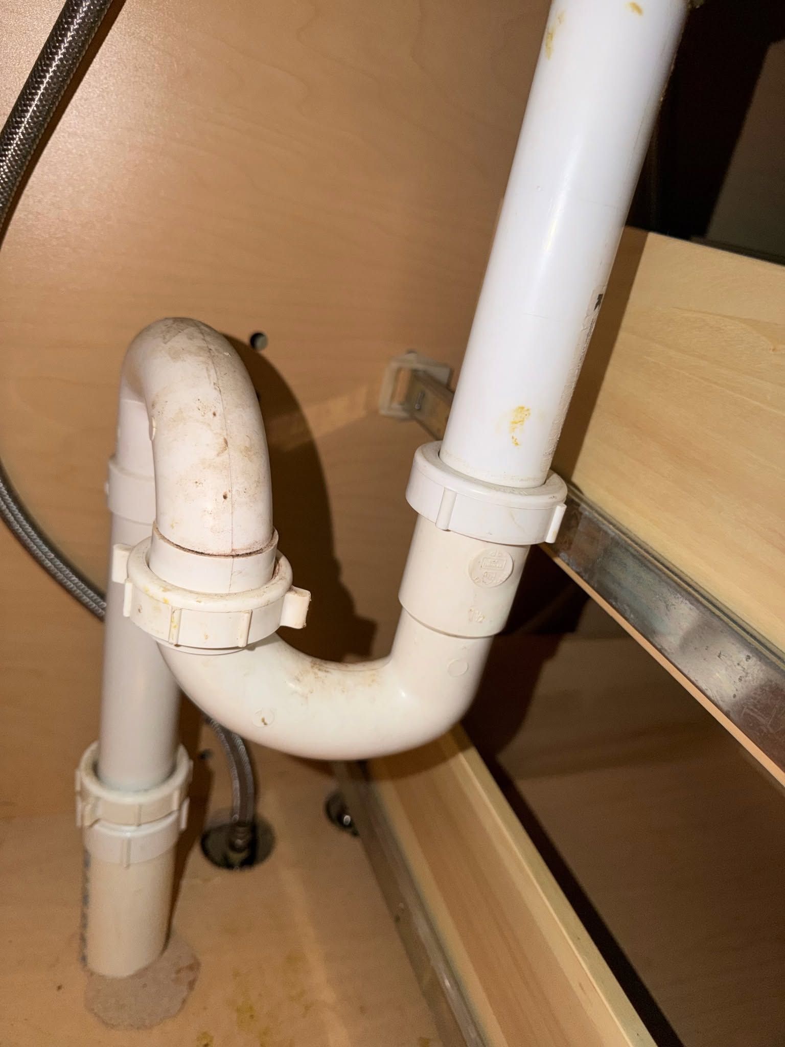 White plumbing drain pipes under a sink cabinet with a U-shaped trap and wood shelves nearby