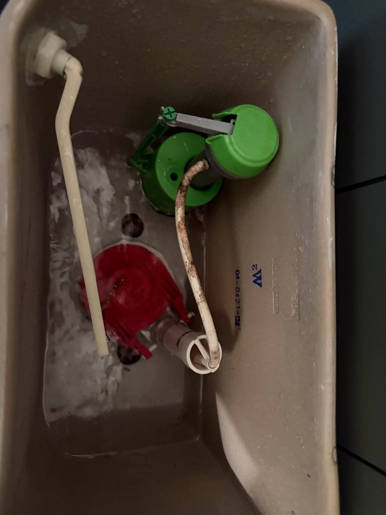 Inside a toilet tank, two float valves—green and red—are connected by white hoses and tubing.