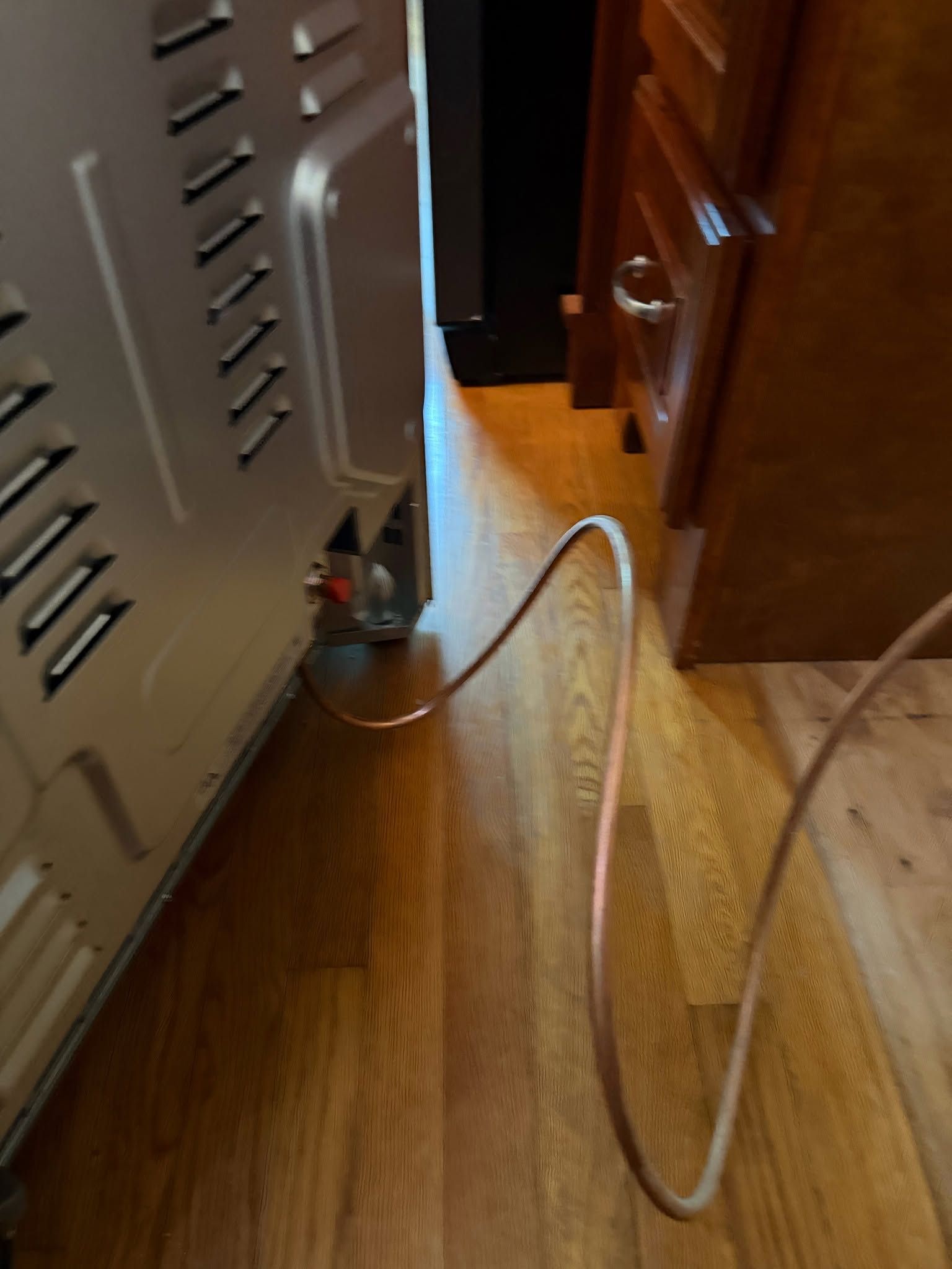 Gray appliance with a white power cord stretched across a wooden floor beside a cabinet opening.