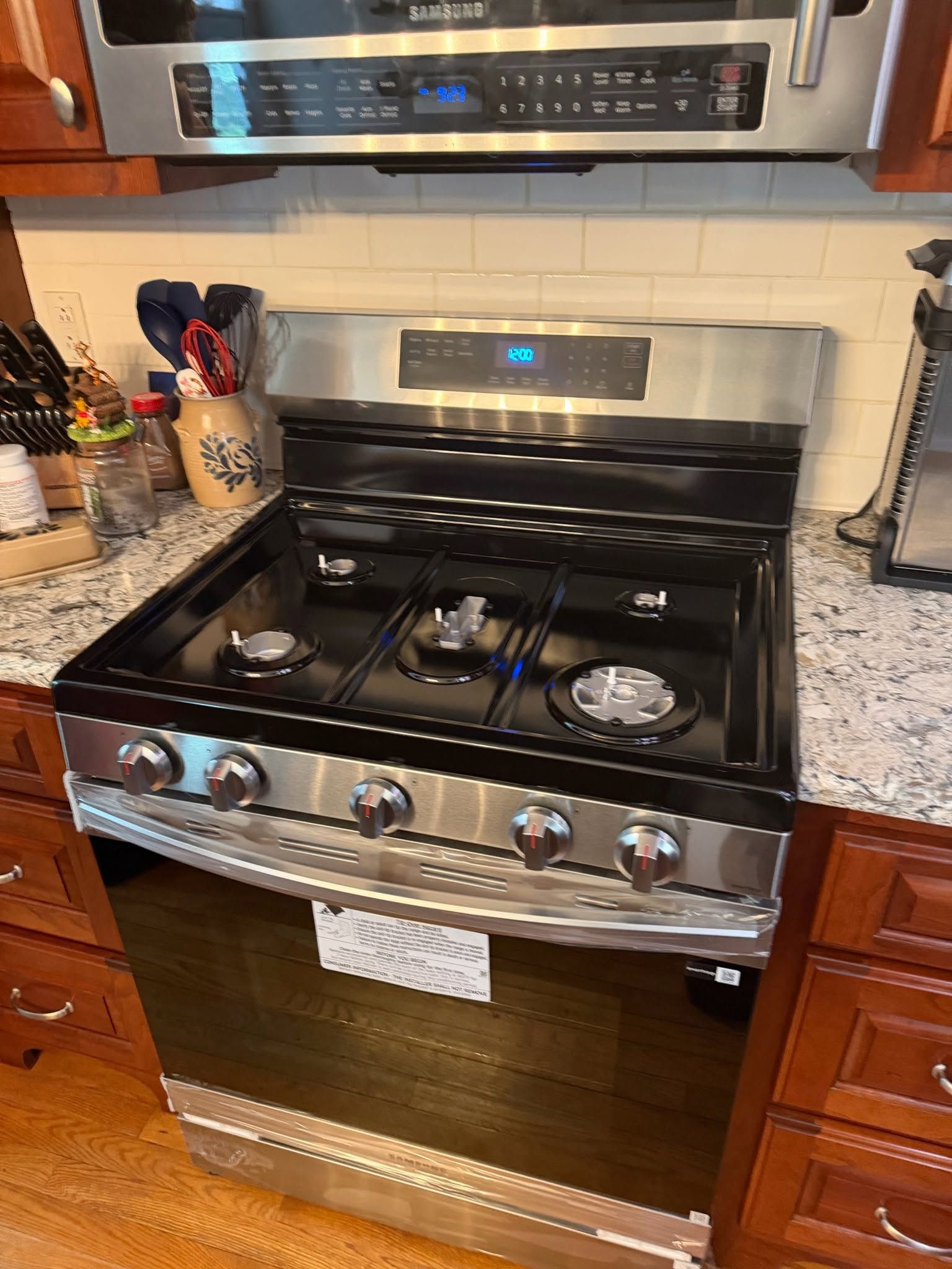 Stainless steel gas range with black cooktop and oven in a kitchen, flanked by wood cabinets and granite counters