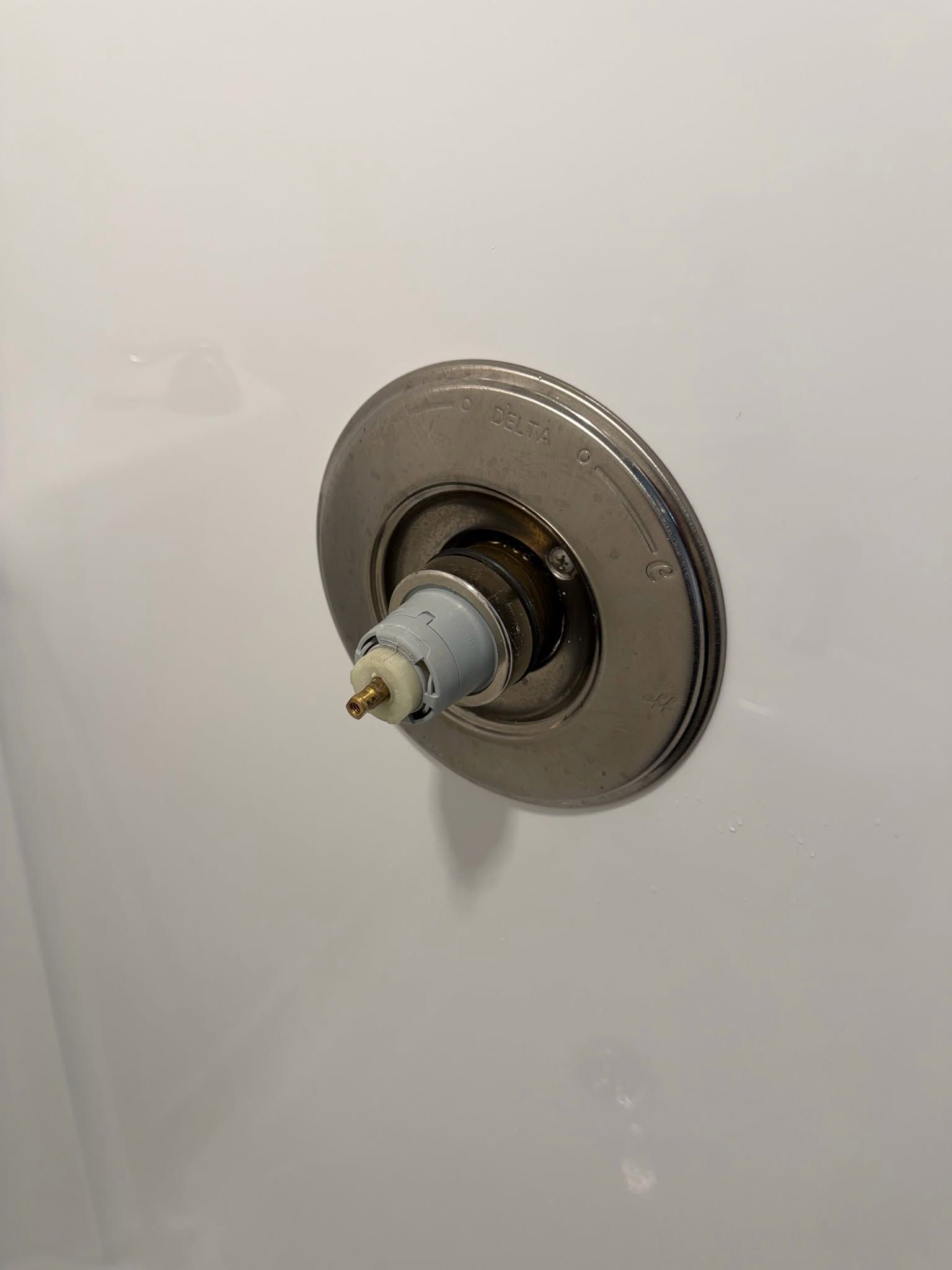 Close-up of a missing shower handle, showing the metal valve stem and circular chrome plate on a white wall