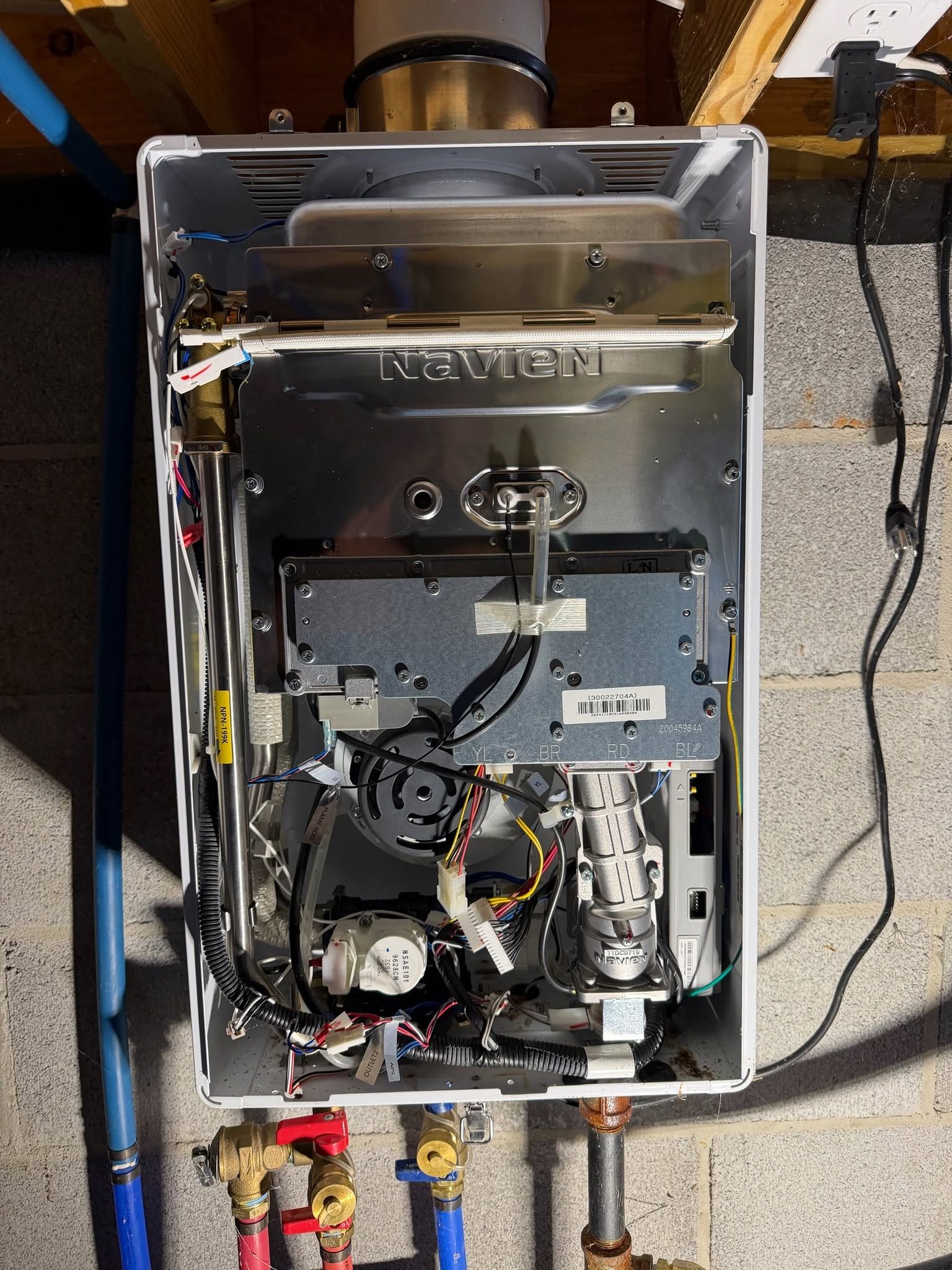 Open furnace with exposed components and visible wiring, pipes below, in a utility room.