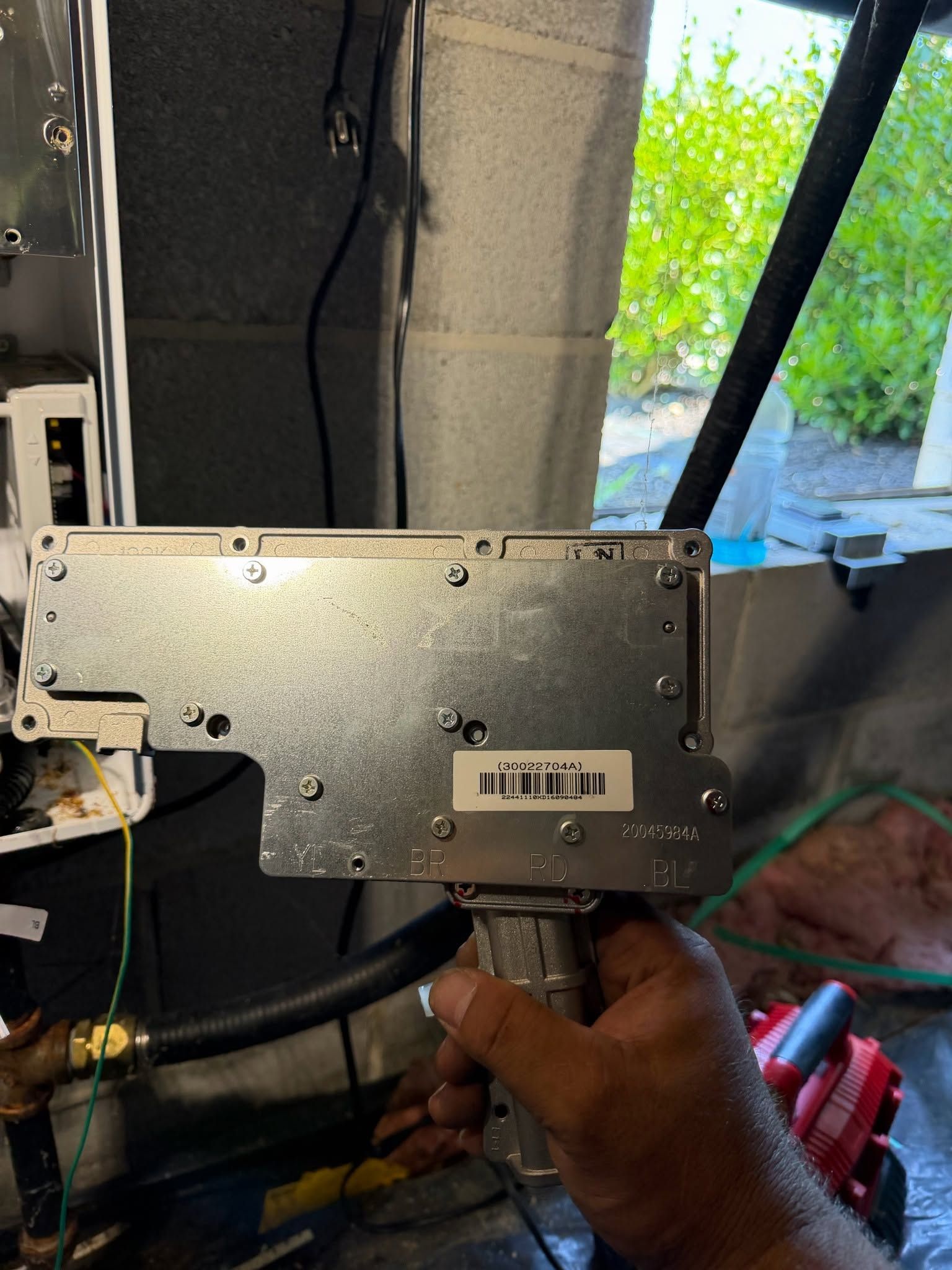 Hand holding a metal electronic module with barcode label in a vehicle interior with tools nearby