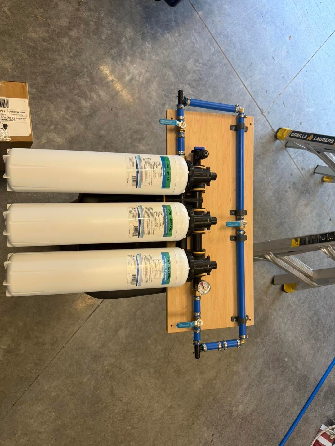 Three white filter cartridges mounted on a blue frame in a workshop on a concrete floor