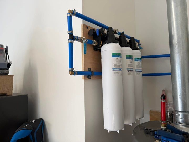 Blue-framed water filtration system with white filter cartridges mounted on a wall.