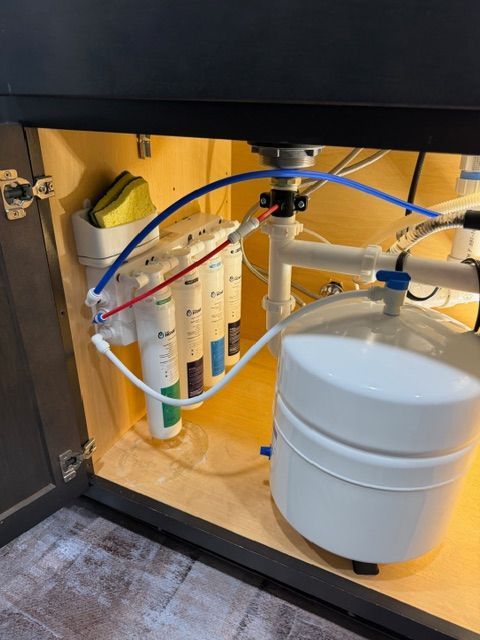 Under-sink water filtration system with white tank, clear filter cartridges, and blue tubing