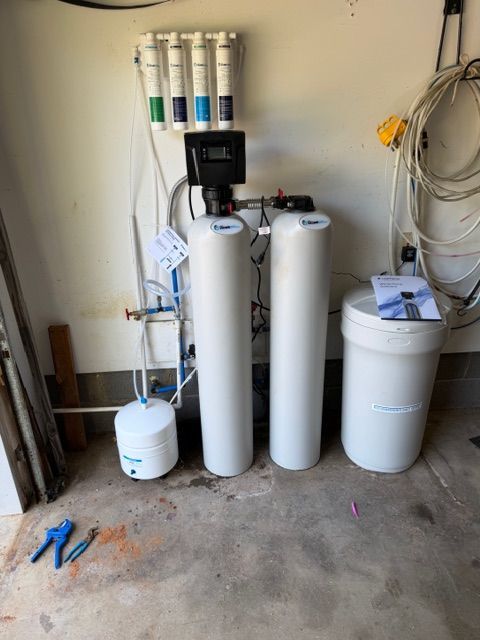 Water filtration system with tanks, filters, and a white storage barrel in a garage-like room