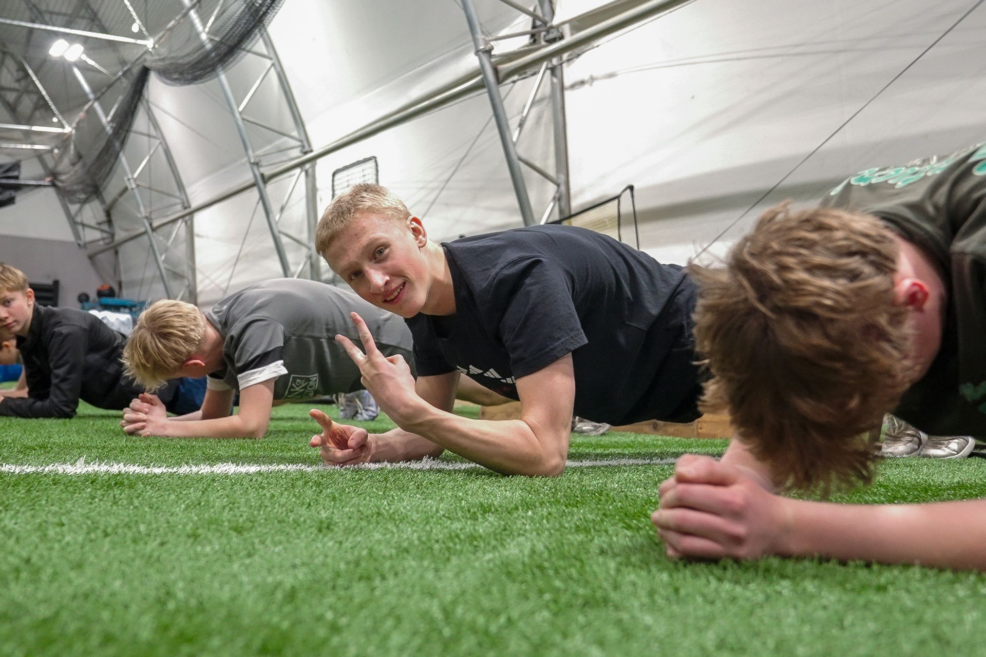People planking on green turf inside a large white tent, one smiling at the camera.