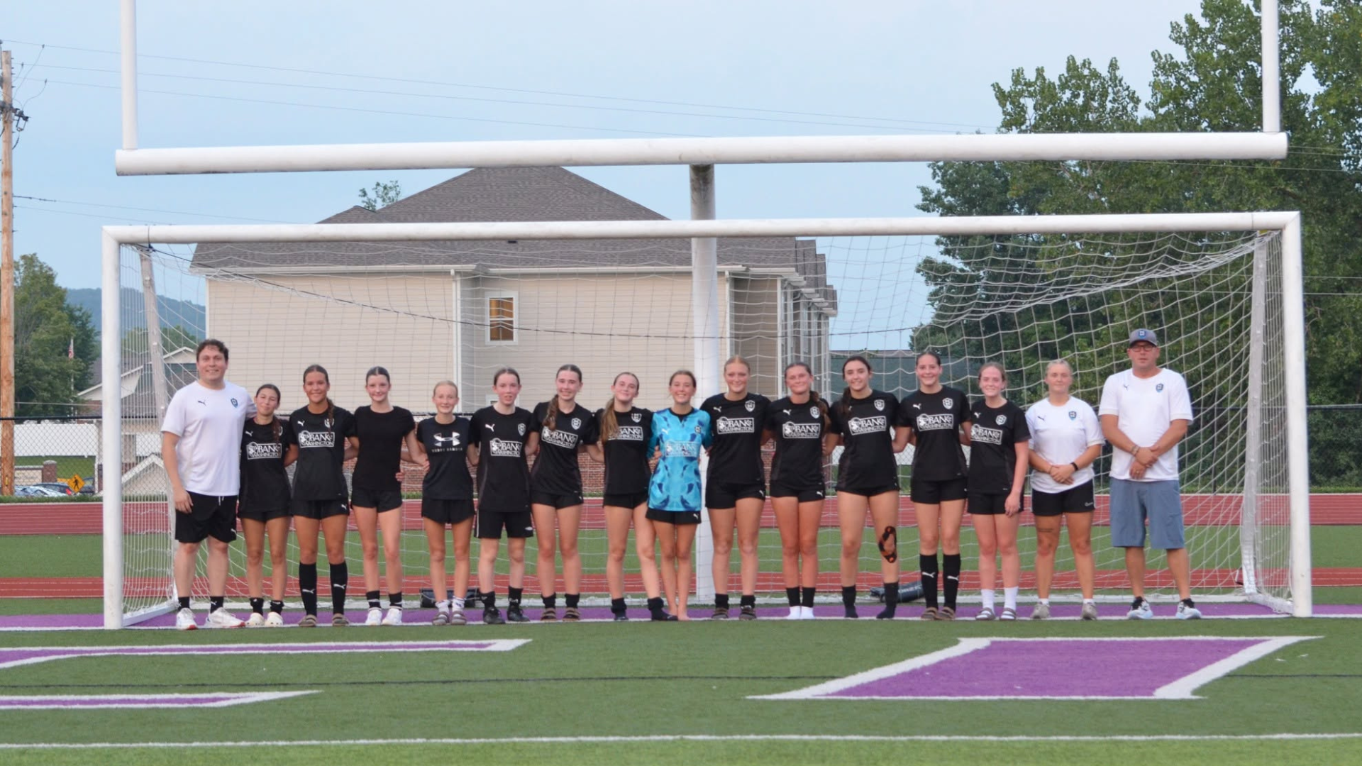 Soccer team posing in front of a goal on a field, wearing black and white uniforms