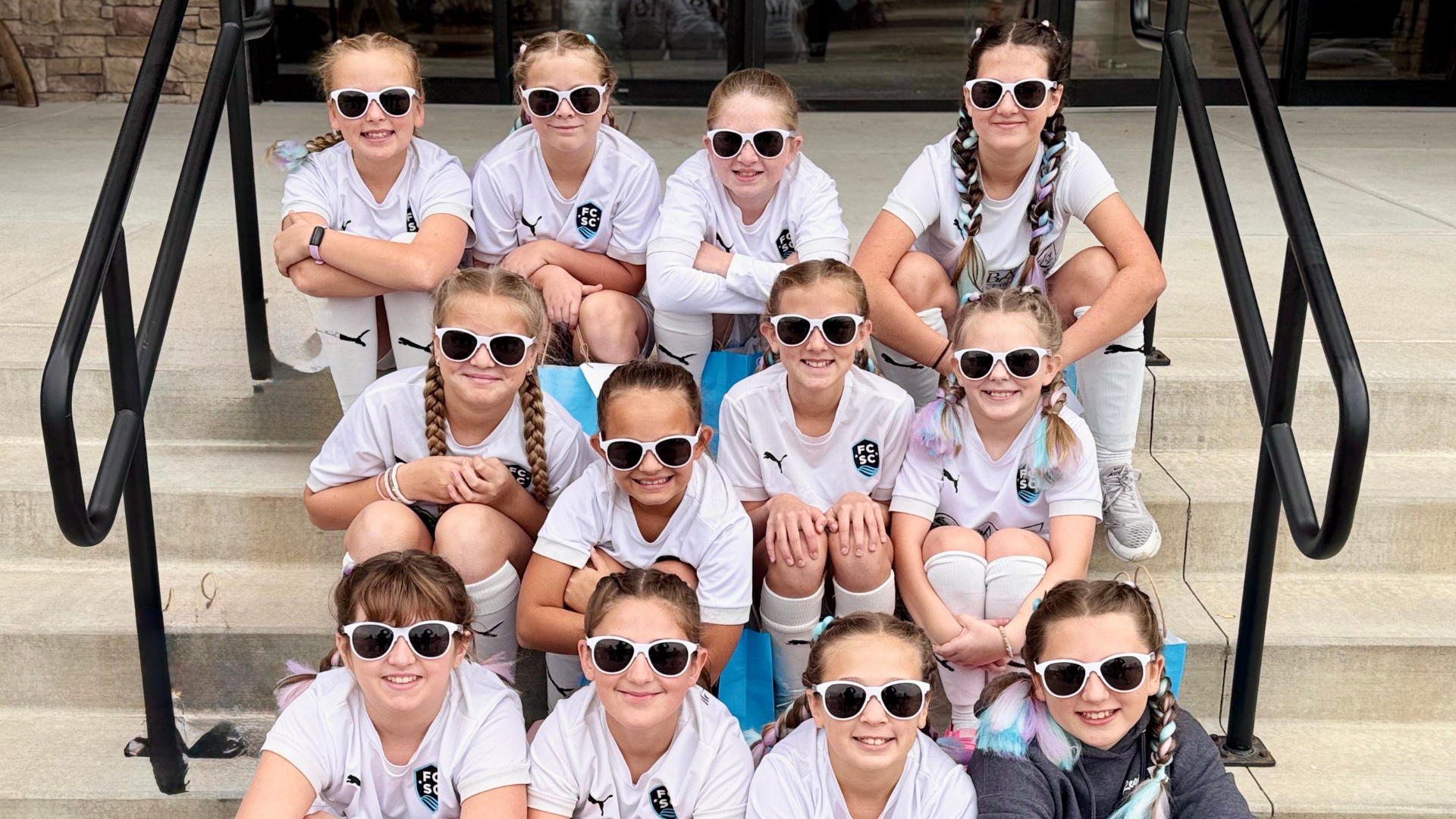 Group of smiling children in sunglasses and white shirts sitting on outdoor steps