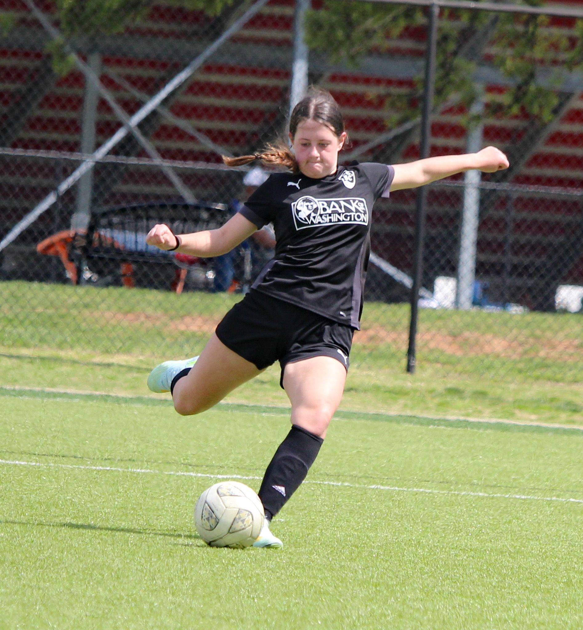 Soccer player in black uniform kicking a ball on a grassy field