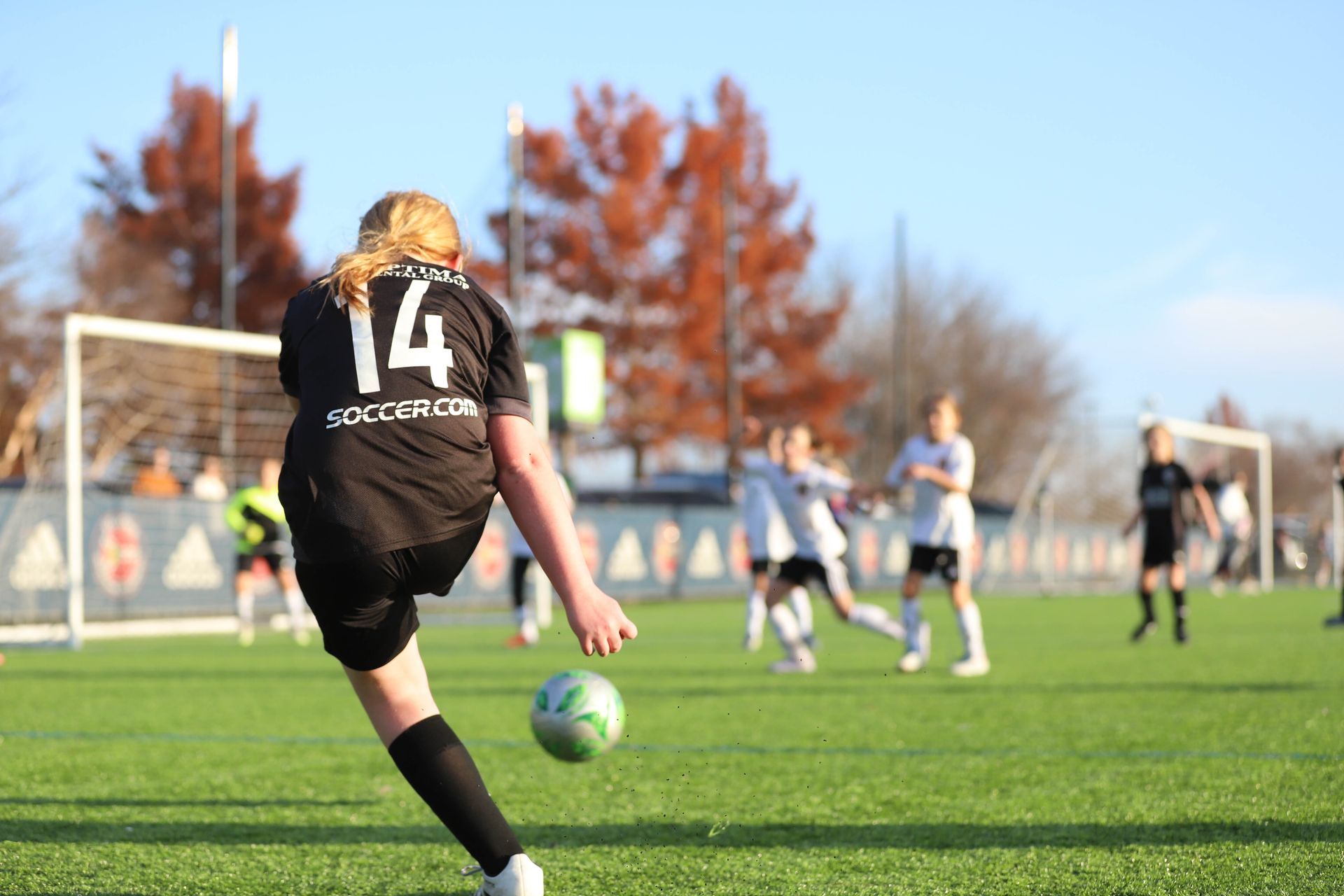 Soccer player in black jersey kicks ball on a grassy field during a match