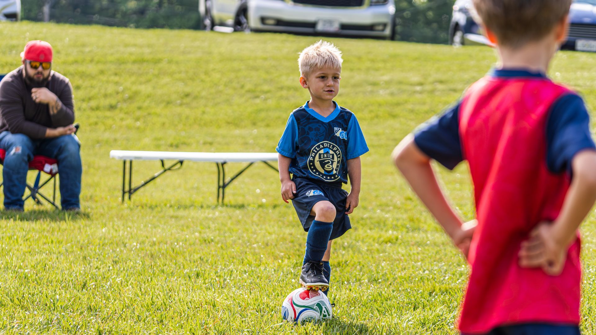 Children playing soccer on a grassy field, with one boy dribbling a ball in the center.