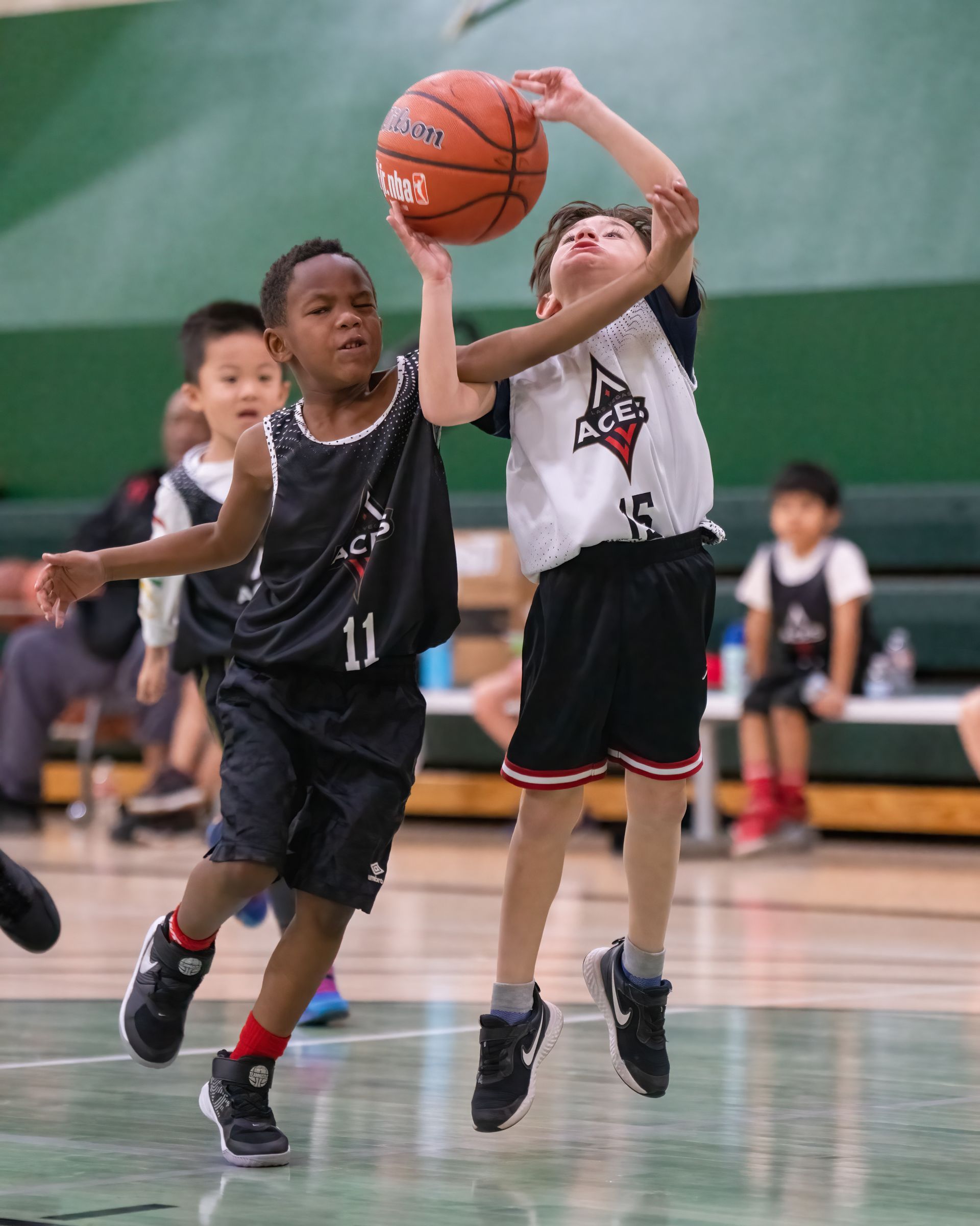 Two youth basketball players leap for a loose ball on an indoor court.