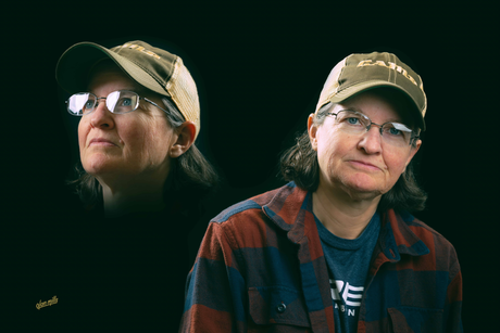 Woman in glasses and baseball cap, wearing a flannel shirt, with a shadow image of herself.