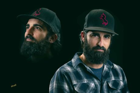 Man wearing a hat and flannel shirt, dark beard, two views against black backdrop.