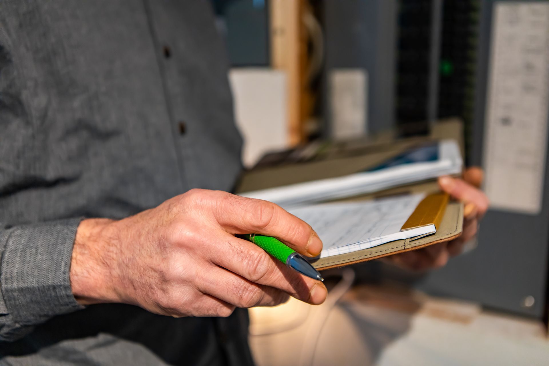 Close-up of a person writing on a clipboard with a green pen in an office setting