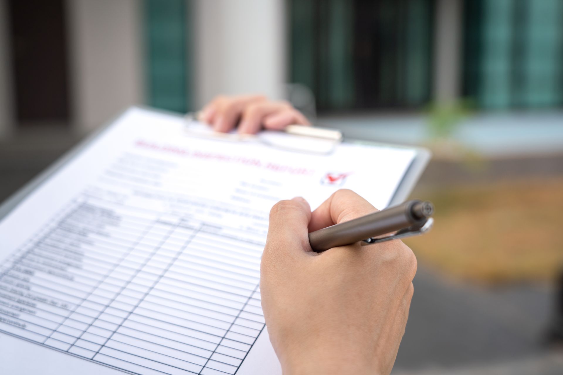 Hand filling out a clipboard form with a pen outdoors
