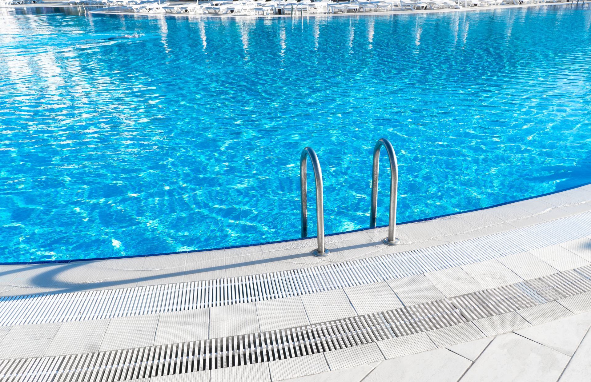 Swimming pool with blue water and a metal ladder beside a white tiled deck