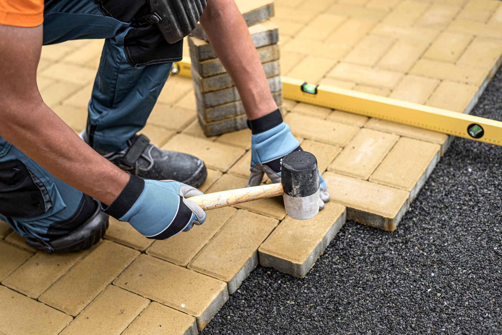 a man is laying bricks on a driveway with a hammer