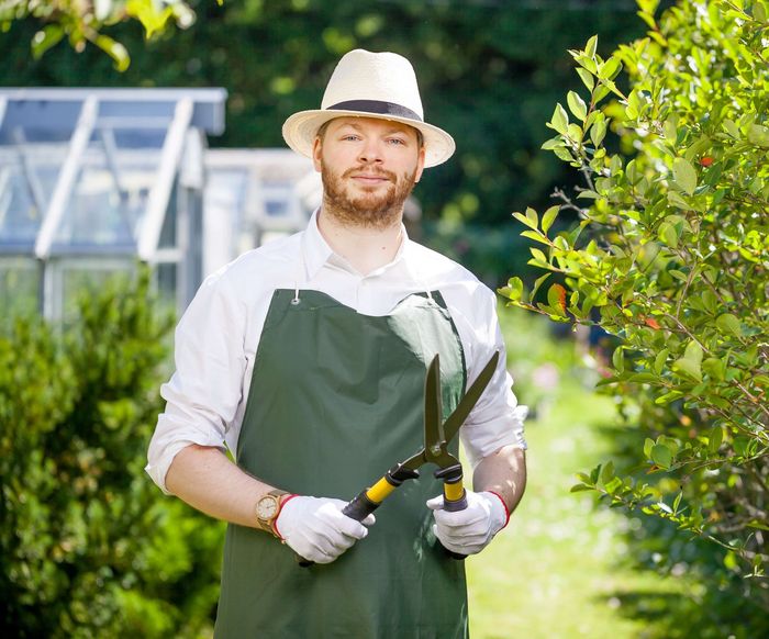 a man in a hat and apron is holding a pair of scissors