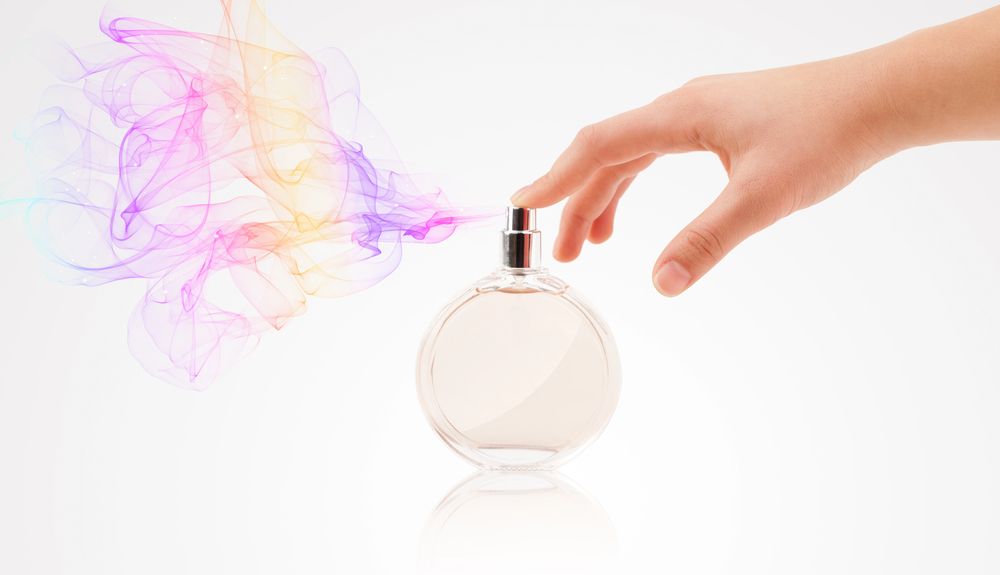 Perfume rociado a mano, con una neblina colorida emanando del frasco. Fondo blanco.