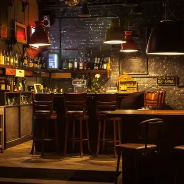 Dimly lit bar interior with stools, liquor bottles, and hanging lights.