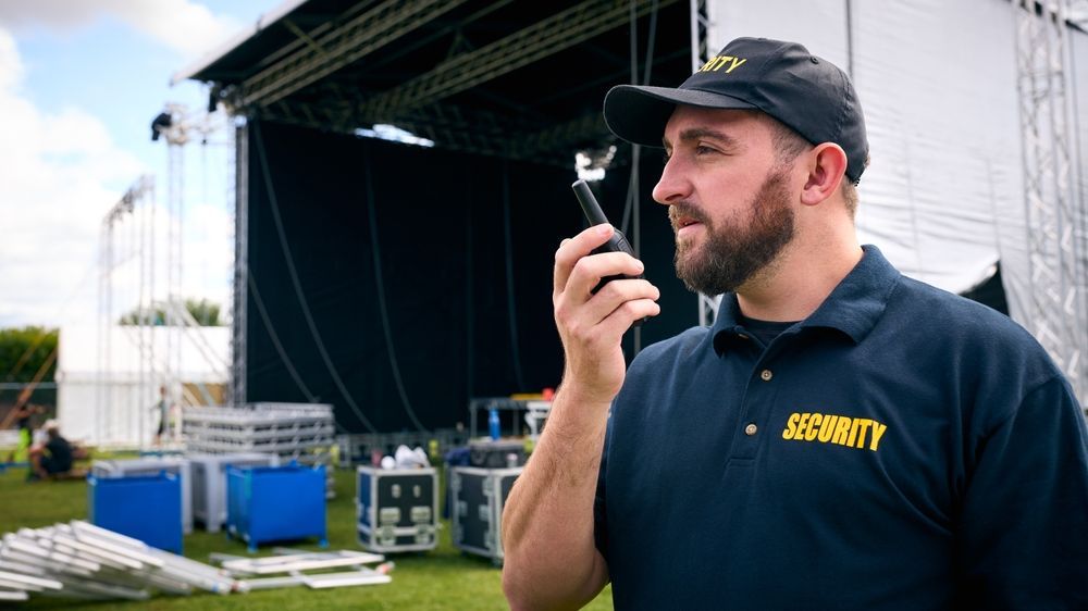 A man is talking on a walkie talkie in front of a stage.