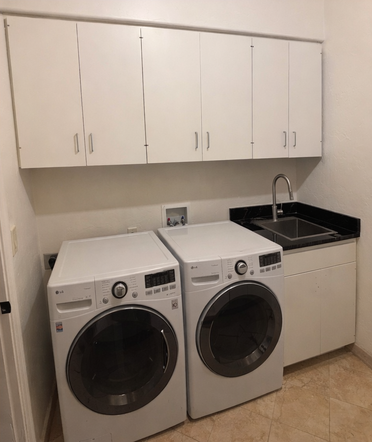 Laundry room with white washer and dryer under cabinets beside a utility sink.
