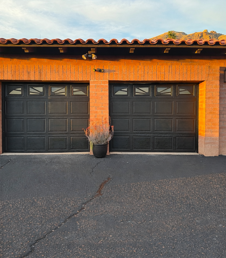 Two black garage doors on an orange stucco house, with a potted plant centered between them.