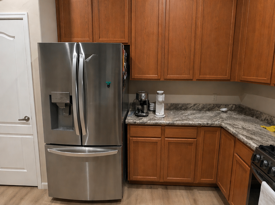 Kitchen corner with stainless steel fridge, wood cabinets, granite counters, and small appliances
