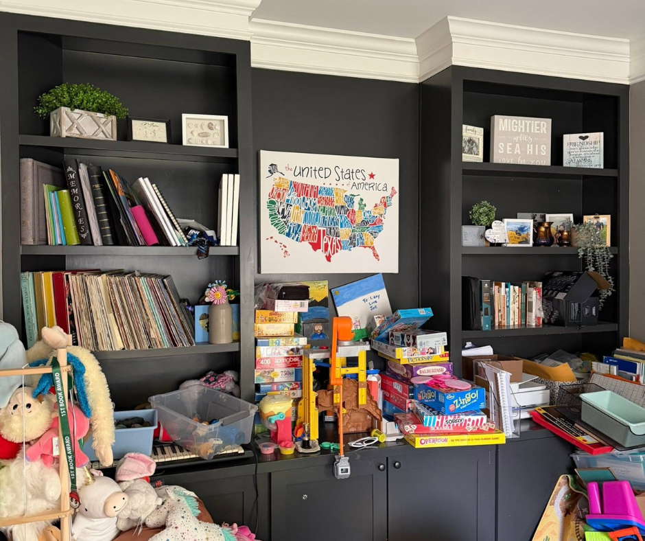 Black shelves and a cluttered tabletop with toys, books, art supplies, and a colorful U.S. map on the wall