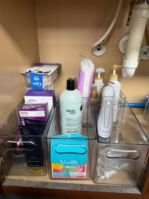 Bathroom cabinet shelf with assorted toiletries, soap dispensers, tissues, and cleaning supplies.