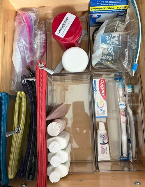 Open drawer of assorted toiletry and makeup items in clear plastic organizers.