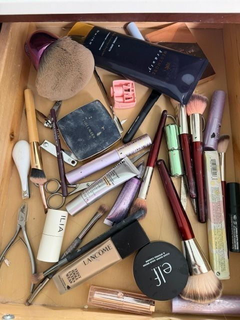 Assorted makeup items and brushes scattered on a wooden surface