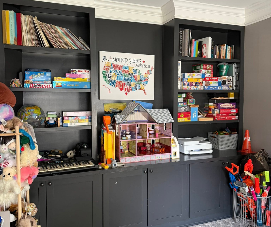 Black built-in shelves with toys, books, and a dollhouse above gray cabinets in a playroom.